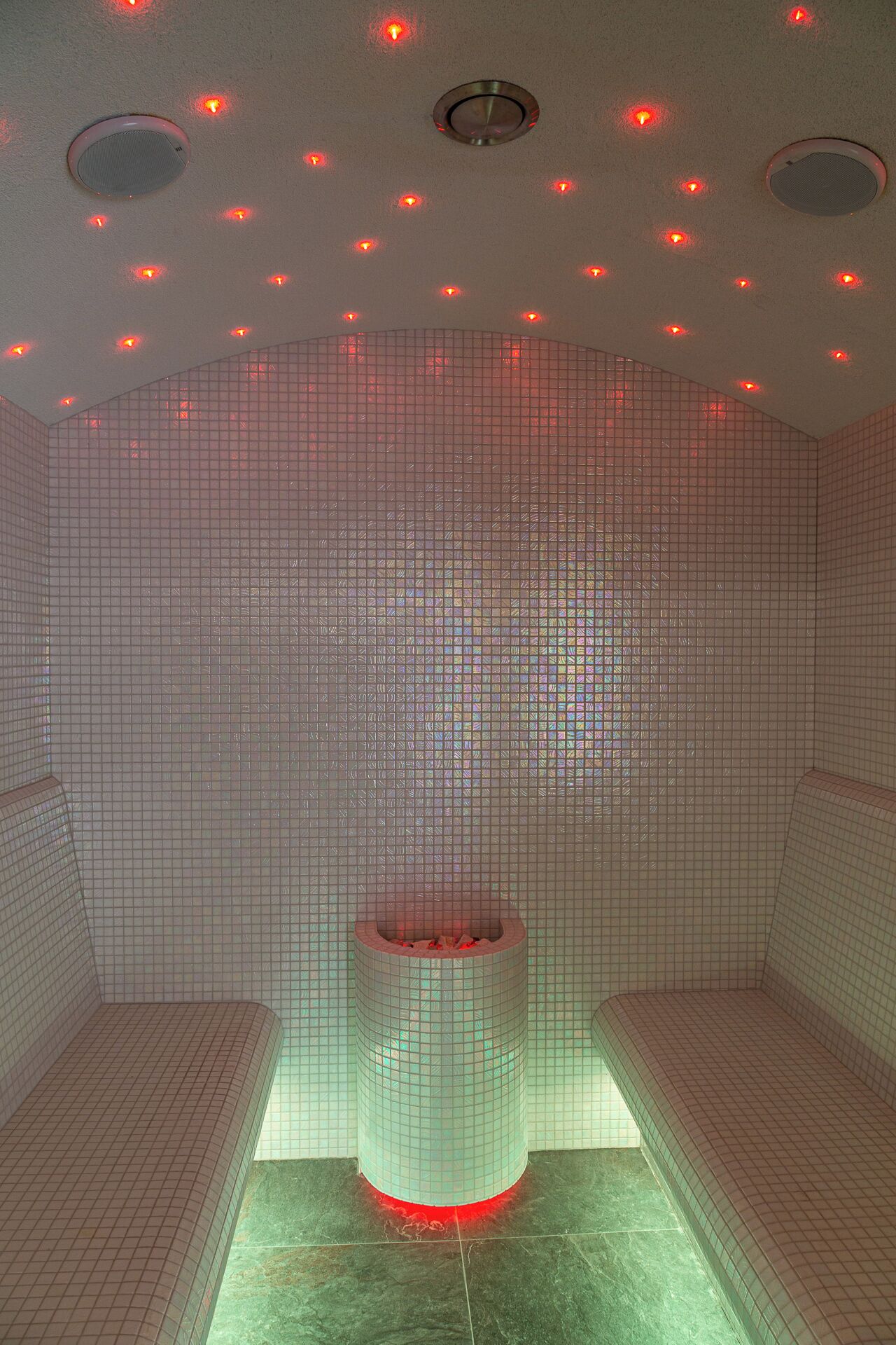 Une pièce avec un mur recouvert de carreaux, une structure cylindrique centrale et de nombreux luminaires au plafond.