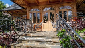 A wooden lodge with stone steps leading to a porch with wicker chairs and a stone fireplace. - Willa Elżbiecina (Zakopane)