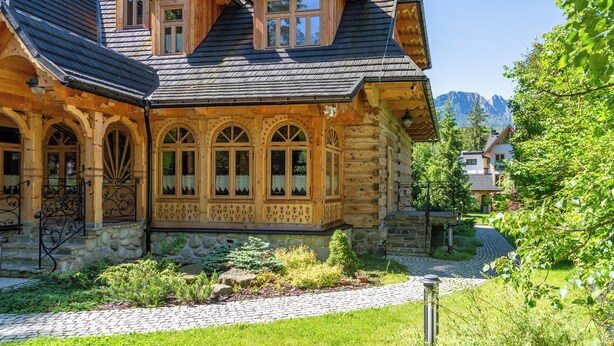A wooden house with a stone foundation, a stone pathway, and a mountain view in the background. - Willa Elżbiecina (Zakopane)