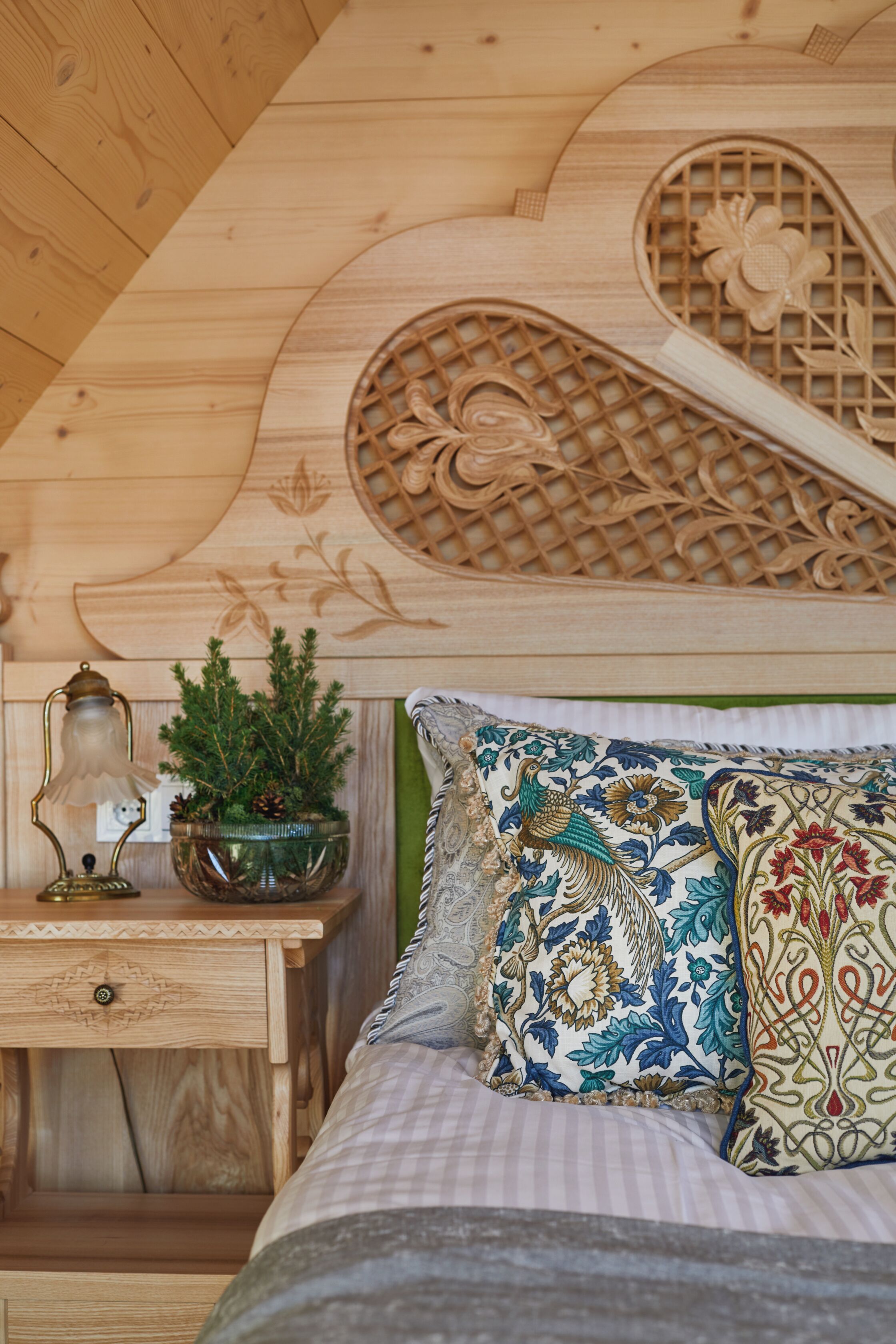 A wooden bed with decorative pillows, a nightstand with a lamp, and a small plant.