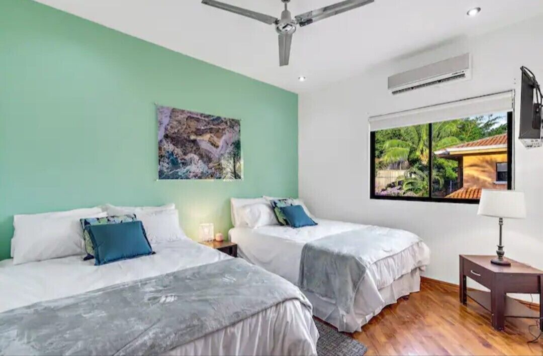 Une chambre avec deux lits, un ventilateur de plafond, une fenêtre donnant sur un paysage verdoyant et un tableau accroché au mur.