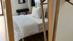 A bedroom with a bed, a bedside table, a mirror, and a window with curtains. - Lokal Ayvalık (Ayvalik)