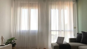 Ein Wohnzimmer mit einer Couch, einem Laptop auf der Couch, einer Holzmannequin und einer Pflanze.