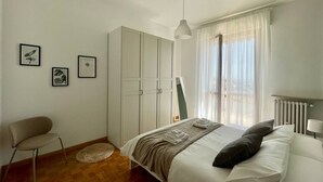 Ein Schlafzimmer mit Bett, Stuhl, Schrank und einem Fenster mit Vorhängen.
