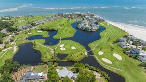 Eine Vogelperspektive eines Golfplatzes mit mehreren Wasserscheiden, einem Strand und Wohngebieten.
