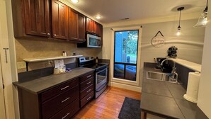 A modern kitchen with wooden cabinets, a built-in microwave, stainless steel appliances, and a window overlooking a deck. - Lakefront Studio Condo (Wright City)