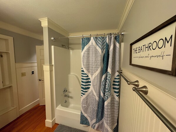 A bathroom with a shower, a bathtub, and a sign that reads "THE BATHROOM please seat yourself."