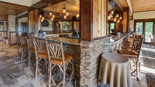 A rustic bar area with stone walls, wooden chairs, and hanging pendant lights. - Lakefront Studio Condo (Wright City)