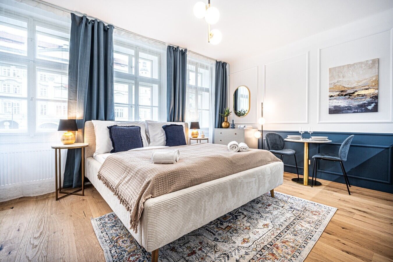 Une chambre d’hôtel moderne, dotée d’un grand lit, d’un petit bureau et offrant une vue sur la ville grâce à de grandes fenêtres.