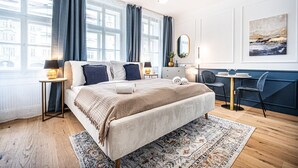 Een moderne hotelkamer met een groot bed, een klein bureau en uitzicht op de stad door grote ramen.