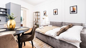 A modern living room with a grey sofa, a dining table with a vase, and a kitchen in the background.