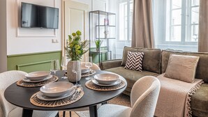 En moderne stue med et rundt spisebord dækket til fire personer, en sofa og et fjernsyn monteret på væggen.