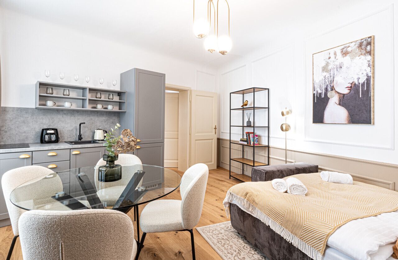 Et moderne hotelværelse med et glasbord, en sofa, en seng med et mønstret tæppe, en reol og et billede på væggen.