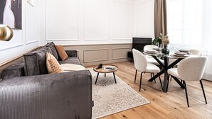 A modern living room with a grey sofa, a round coffee table, and a dining area with a glass table and white chairs.