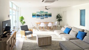 Una sala de estar moderna con televisor, sofá, mesa de comedor, sillas y obras de arte en la pared.