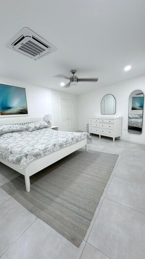 Ein Schlafzimmer mit einem Bett, einem Schminktisch, einem Deckenventilator, einem Wandspiegel und einem Gemälde.