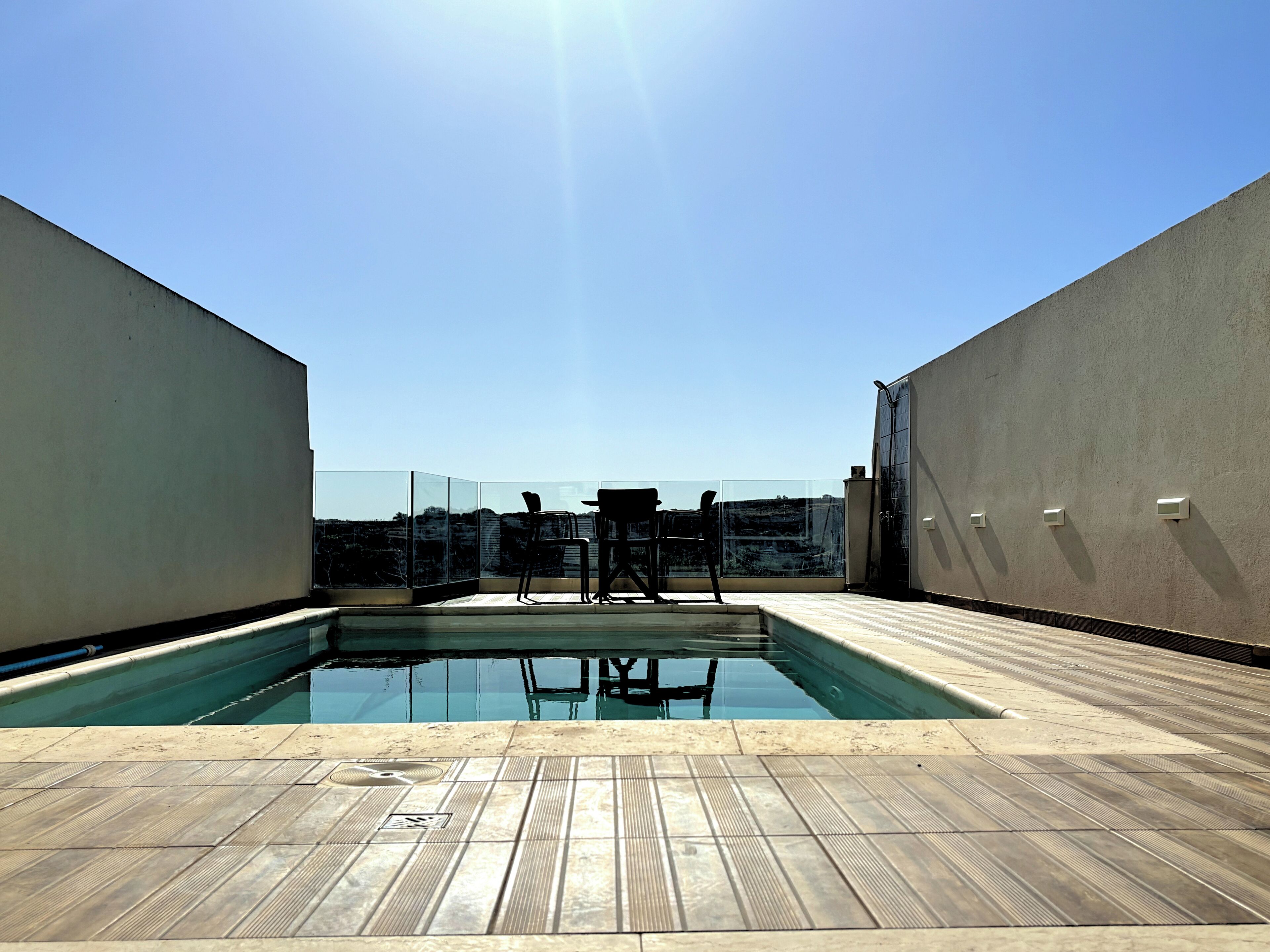 A rooftop pool area with a clear view of the city skyline, a glass partition, and a seating arrangement.