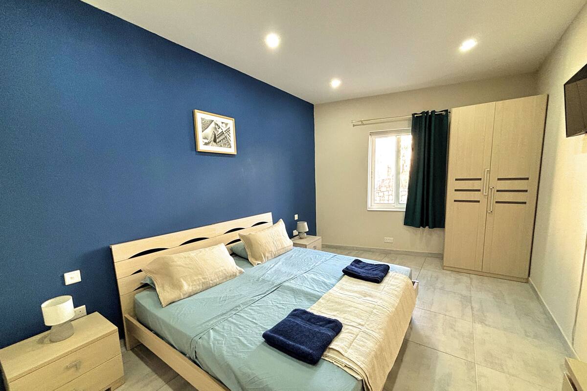 A bedroom with a bed, nightstands, a wardrobe, and a window with curtains.