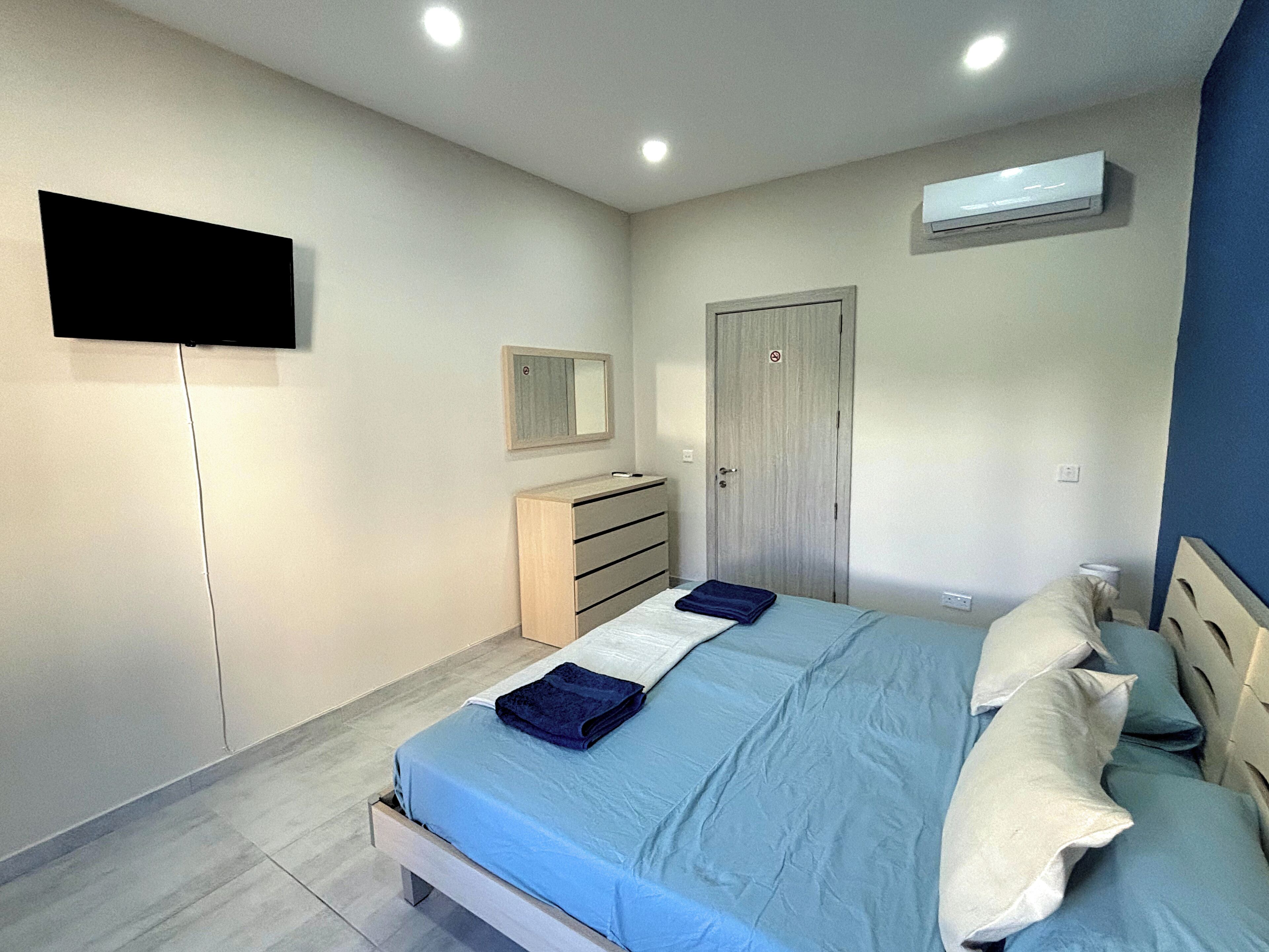 A bedroom with a bed, a dresser, a mirror, and a TV mounted on the wall.