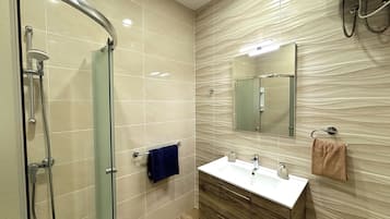 Un baño moderno con cabina de ducha de vidrio, tocador con lavabo y espejo, y perchero para toallas.