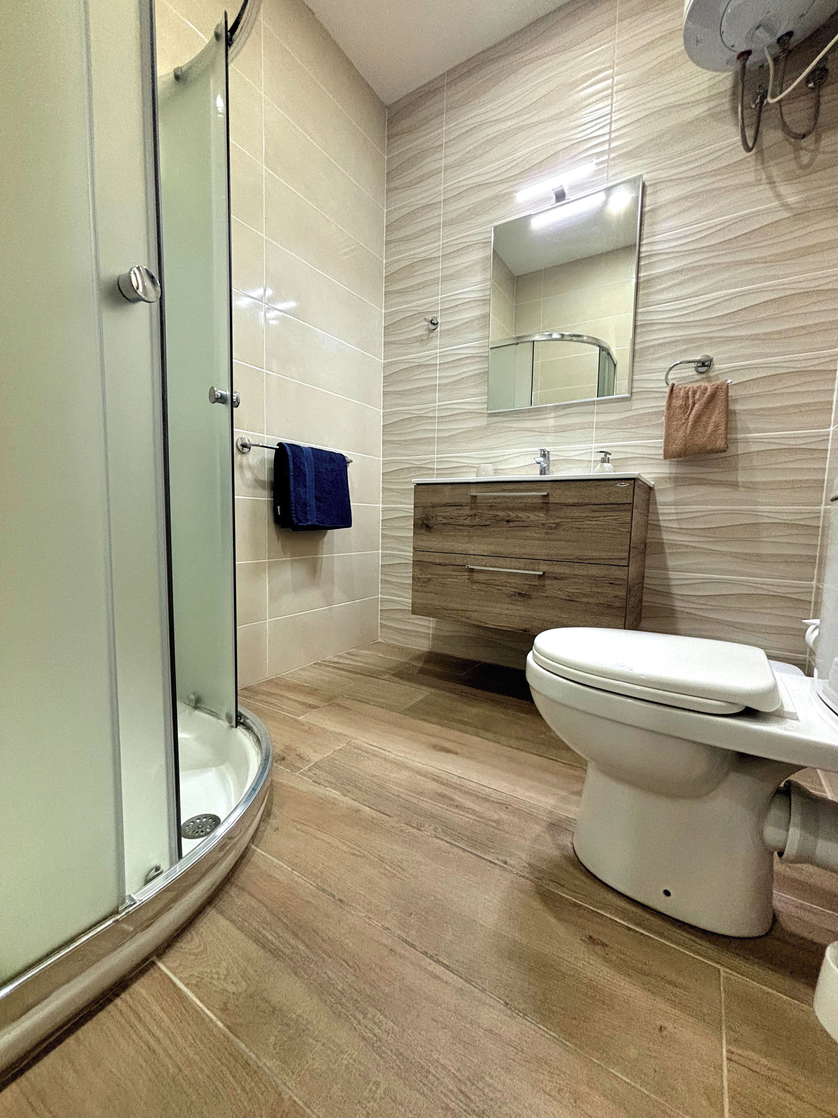 Un baño moderno con cabina de ducha de vidrio, tocador de madera y un inodoro blanco.