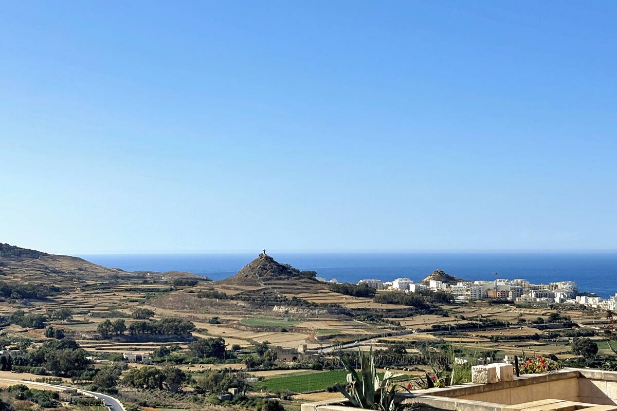 A coastal landscape with a hill, buildings, and a clear sky.