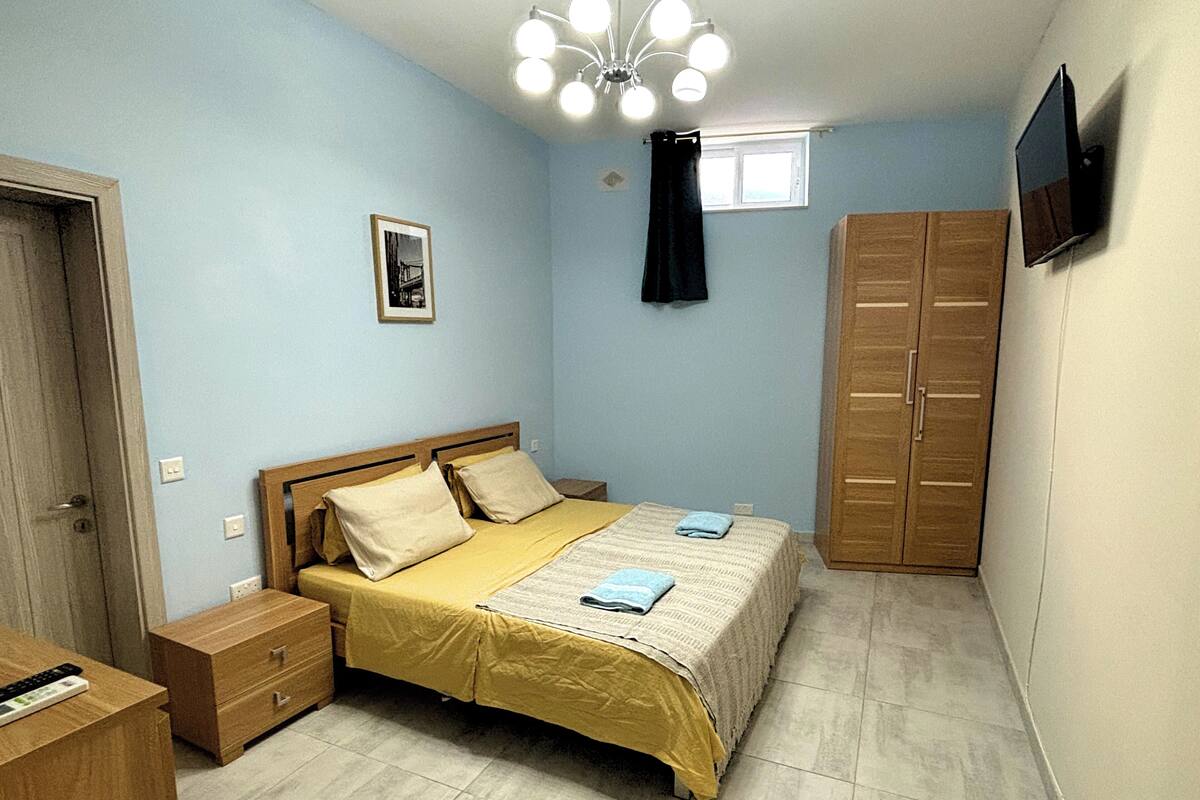 A bedroom with a bed, nightstand, wardrobe, and a TV on the wall.