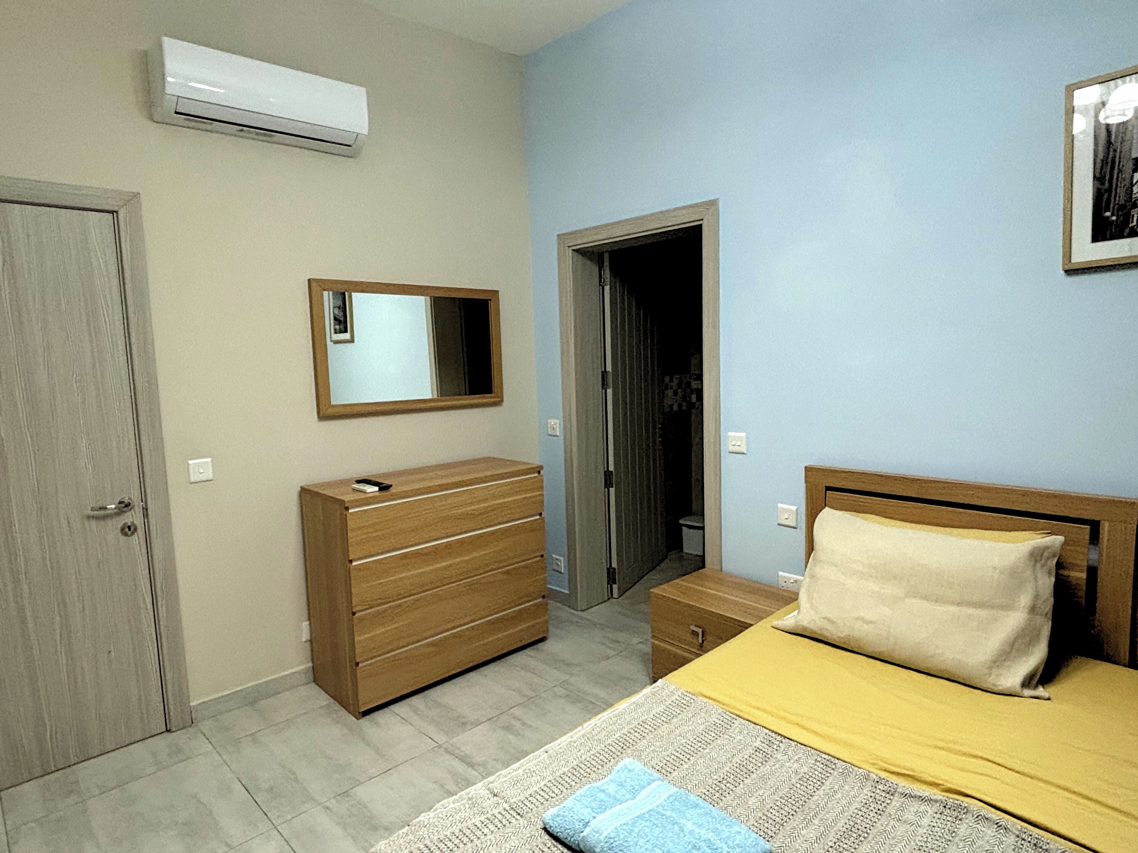 Un dormitorio con cama, cómoda, espejo y equipo de aire acondicionado.