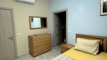 A bedroom with a bed, a dresser, a mirror, and an air conditioning unit.