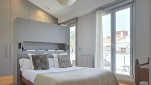 A modern bedroom with a large bed, grey walls, and a view of the city through a sliding glass door. - Boulevard Terrace by FeelFree Rentals (Donostia)