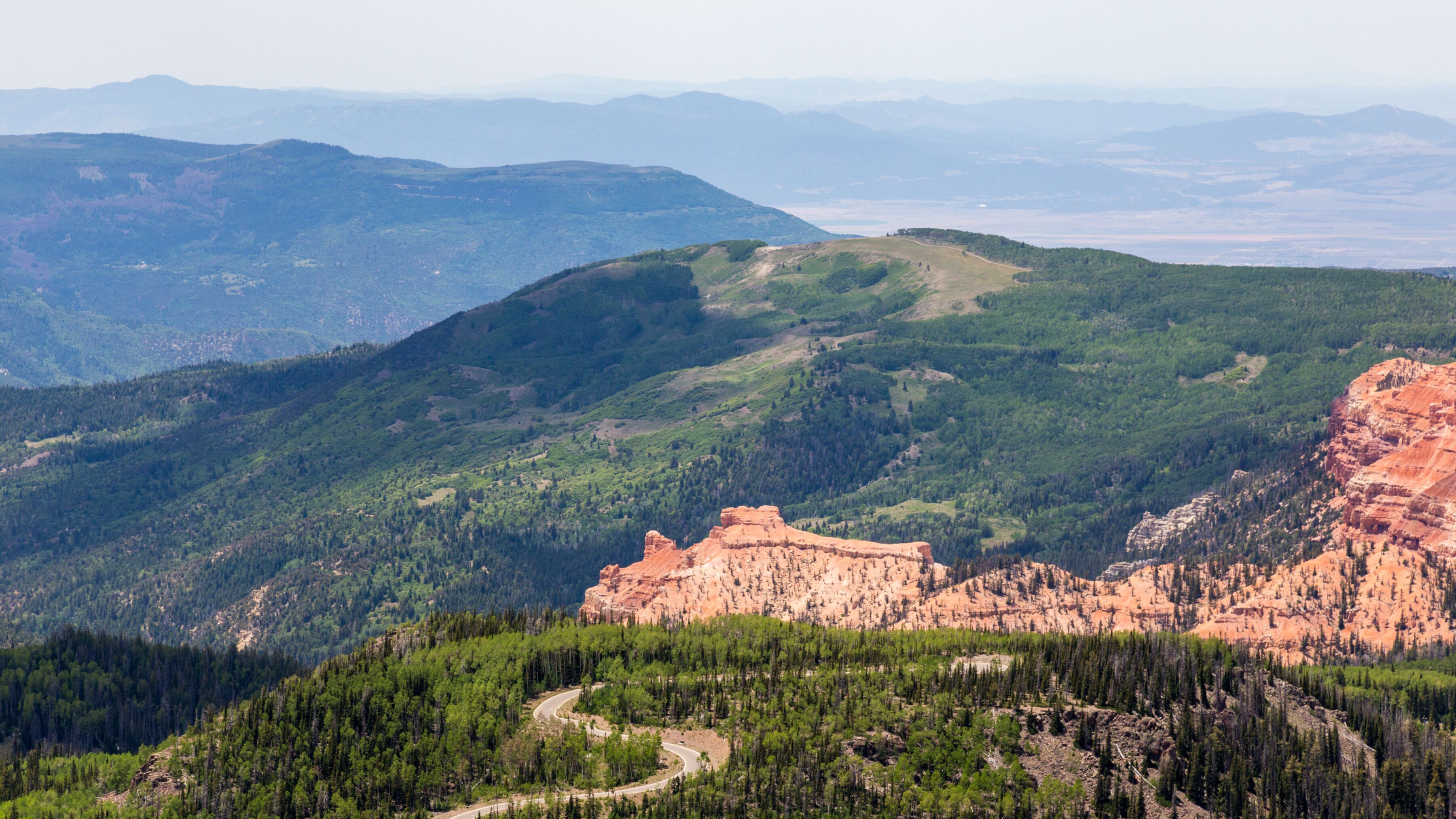 Un paysage montagneux avec une route sinueuse et une formation rocheuse rouge imposante.