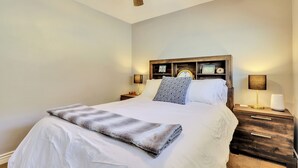 Ein ordentlich bezogenes Bett mit grauer Decke, einem hölzernen Kopfteil, Nachttischlampen und einem Deckenventilator.