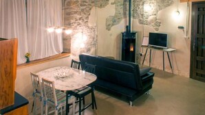 Een gezellige woonkamer met een stenen muur, een open haard, een zwarte bank, een ronde tafel met stoelen en een televisie op een dressoir.