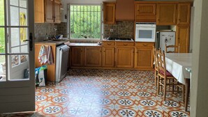 A kitchen with wooden cabinets, a tiled floor, a window with bars, and a hanging light fixture. - Mas Cévenol à Proximité du Village et de la Rivière (Lasalle)