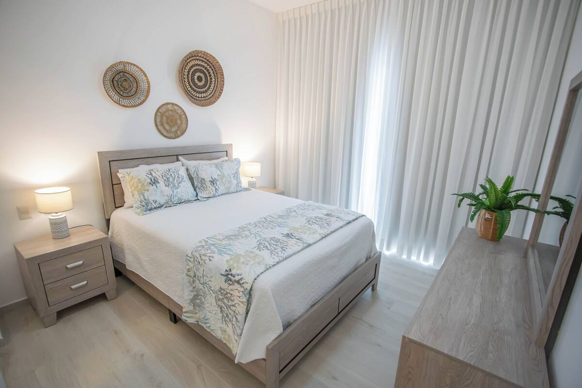 Une chambre à coucher avec un lit, des tables de chevet, une commode et une plante en pot.