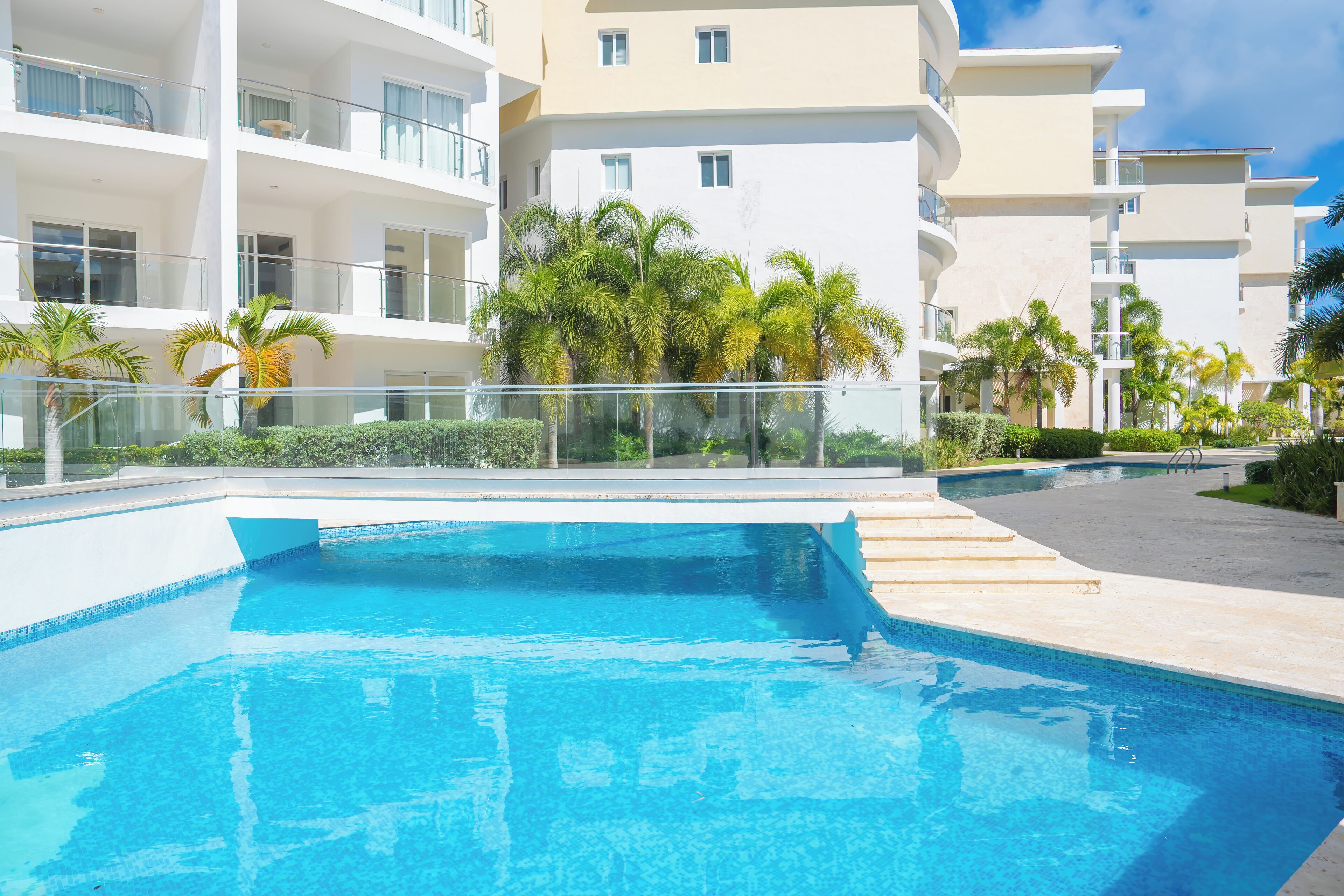 Ein modernes Hotel mit Schwimmbad, mehreren Balkonen und Palmen.