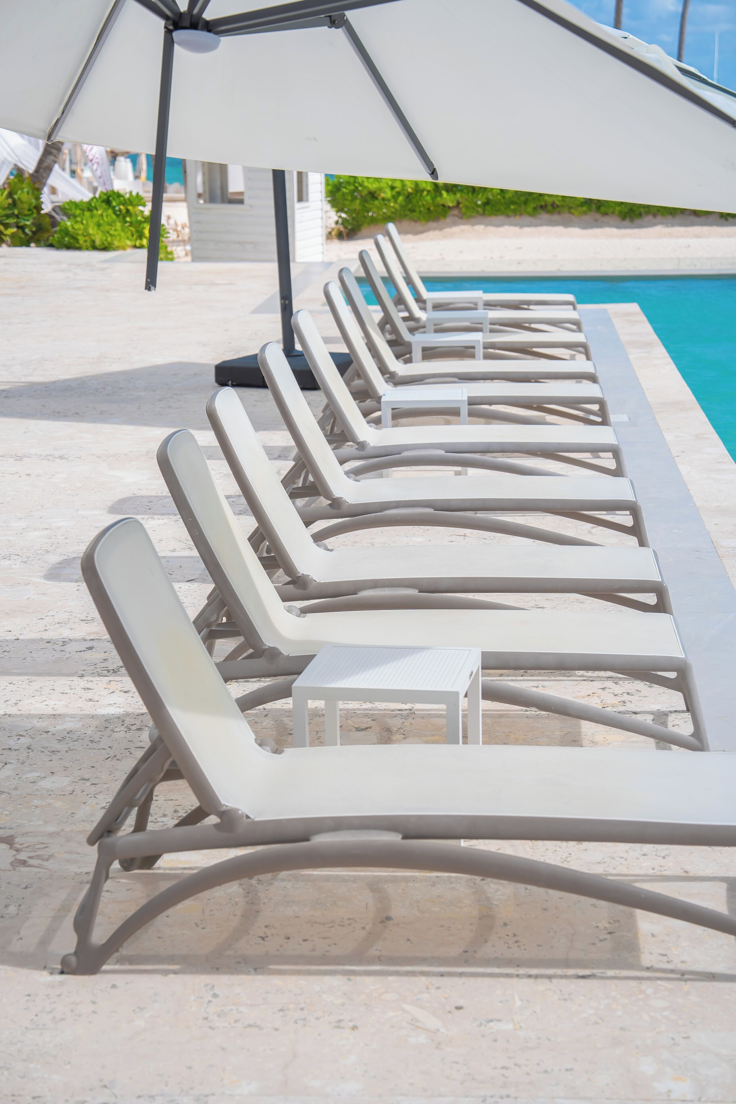 Eine Reihe weißer Liegestühle und ein Tisch am Pool, mit einem Strandbienenstock darüber.