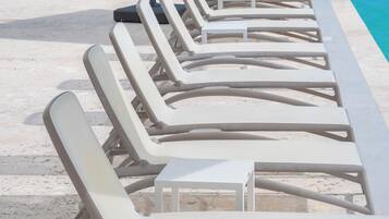 Eine Reihe weißer Liegestühle und ein Tisch am Pool, mit einem Strandbienenstock darüber.