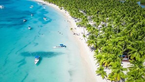A beach with clear turquoise waters, palm trees, and boats. - Xeliter Playa Coral Bavaro (Punta Cana)