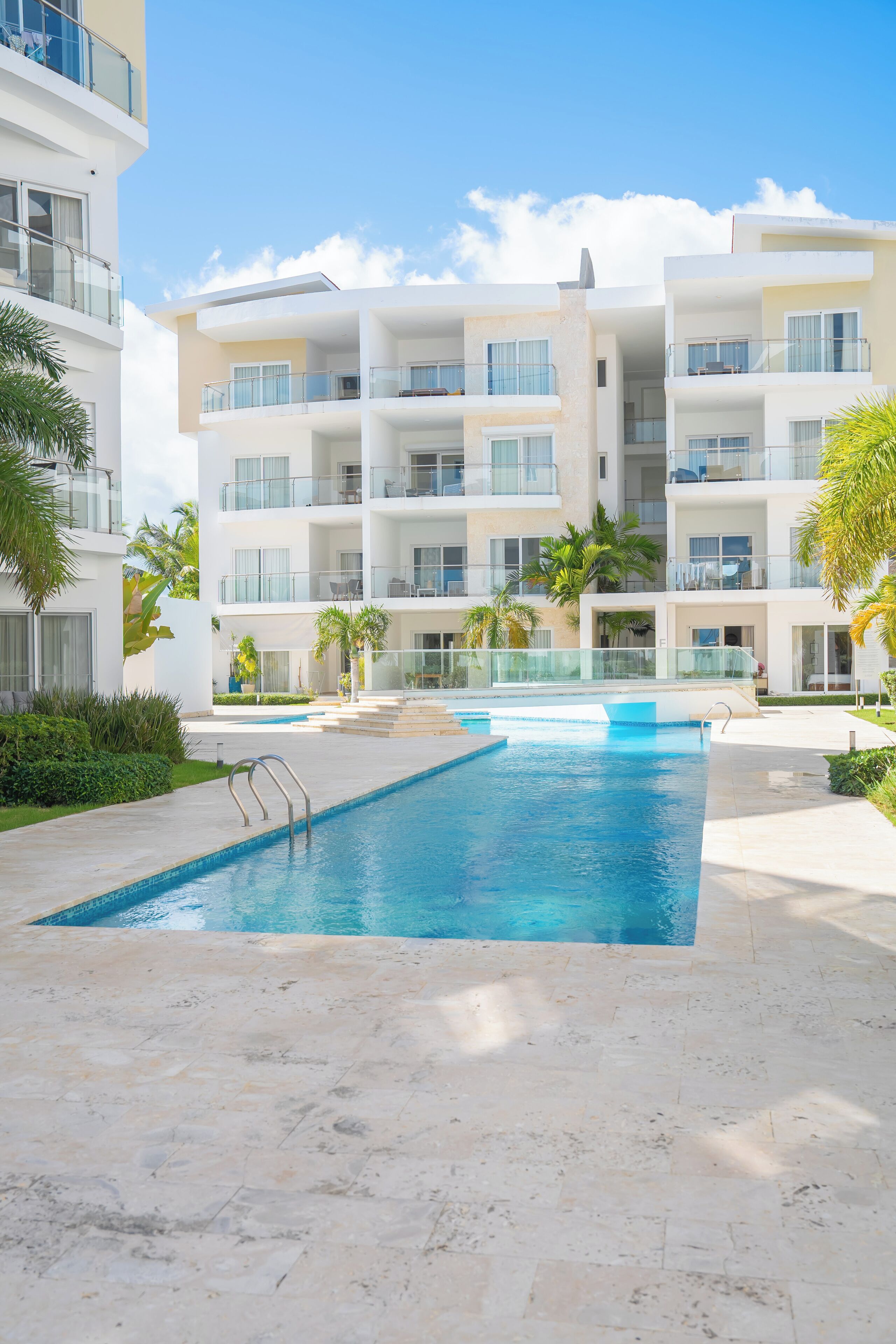 A modern hotel with a swimming pool, multiple balconies, and a clear blue sky.