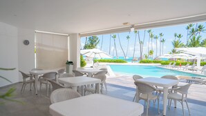 A poolside area with white wicker furniture, a view of the ocean, and palm trees. - Xeliter Playa Coral Bavaro (Punta Cana)