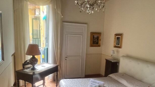 A hotel room with a bed, a desk, a chair, a lamp, a chandelier, and a door.
