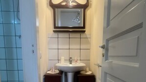 A bathroom with a white sink, two dark wooden side tables, a mirror above the sink, and a red patterned rug on the floor.