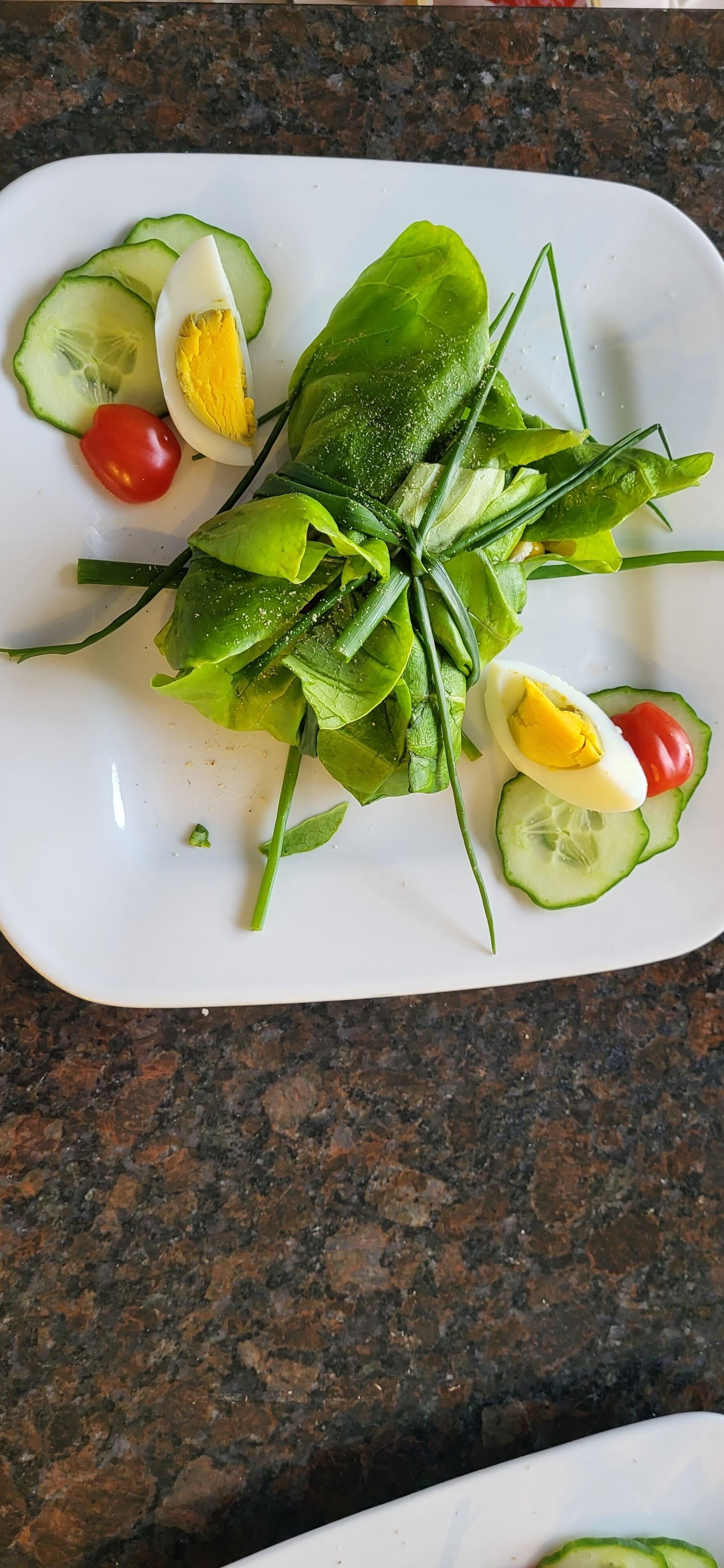 A white plate with a salad consisting of spinach, cucumber slices, cherry tomatoes, and a halved boiled egg.