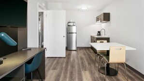 A modern kitchen with a white countertop, stainless steel refrigerator, and a dining area with a white table and chairs. - Studio 6 Tempe, AZ – Elliot Road (Tempe)