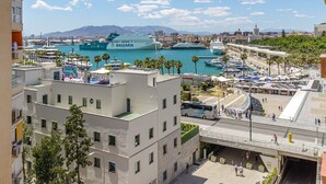 Näkymä rannikkokaupunkiin, jossa satamassa on ankkuroituna risteilyalus nimeltä ’BALEARIA’. Kaupungissa on moderneja rakennuksia, joissa on parvekkeita, jalankulkijoiden käytävä ja silta.