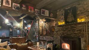 A cozy room with a stone fireplace, a leather chair, a coffee table, and a wall adorned with posters and guitars. - Grunberg Haus Inn & Cabins (Waterbury)