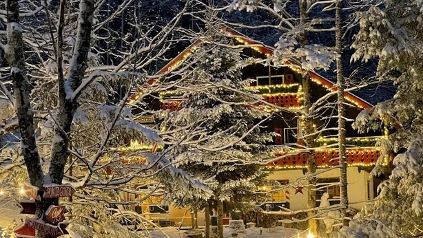 A snow-covered landscape with a building adorned with string lights and illuminated signs pointing to various destinations. - Grunberg Haus Inn & Cabins (Waterbury)