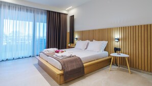 A modern hotel room with a large bed, a bedside table, and a view of the city through sheer curtains. - Aura Luxury Suites - Olympiada Cozy Getaways (Aristotelis)