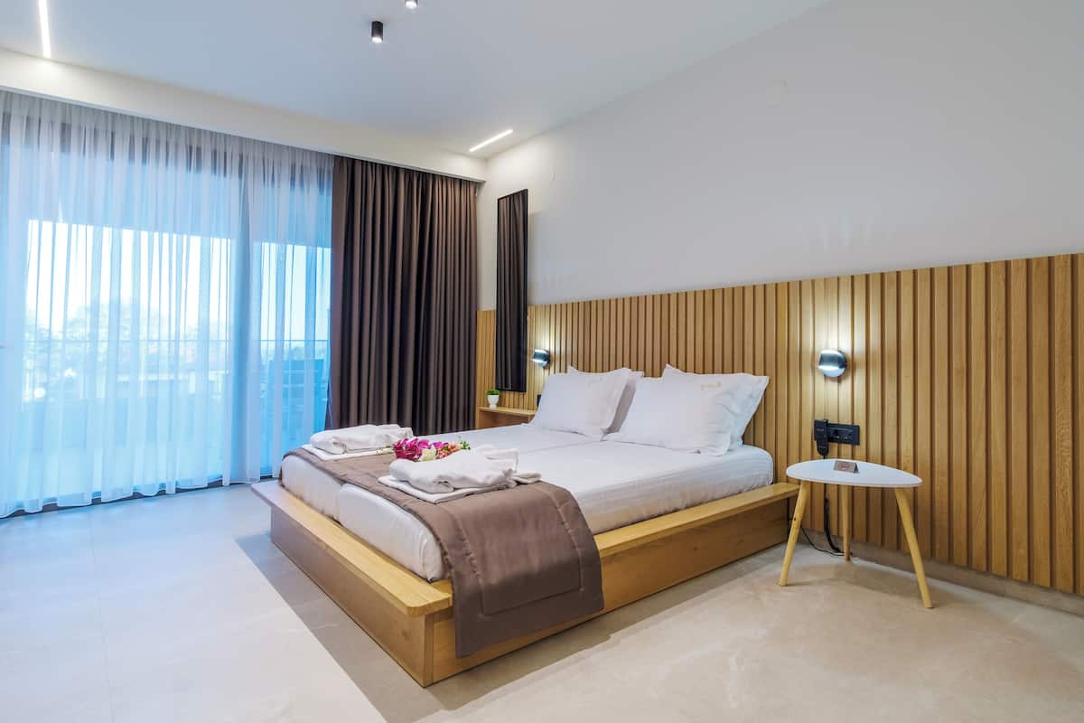 Una habitación de hotel moderna con una cama grande, una mesita de noche y vistas de la ciudad a través de cortinas traslúcidas.